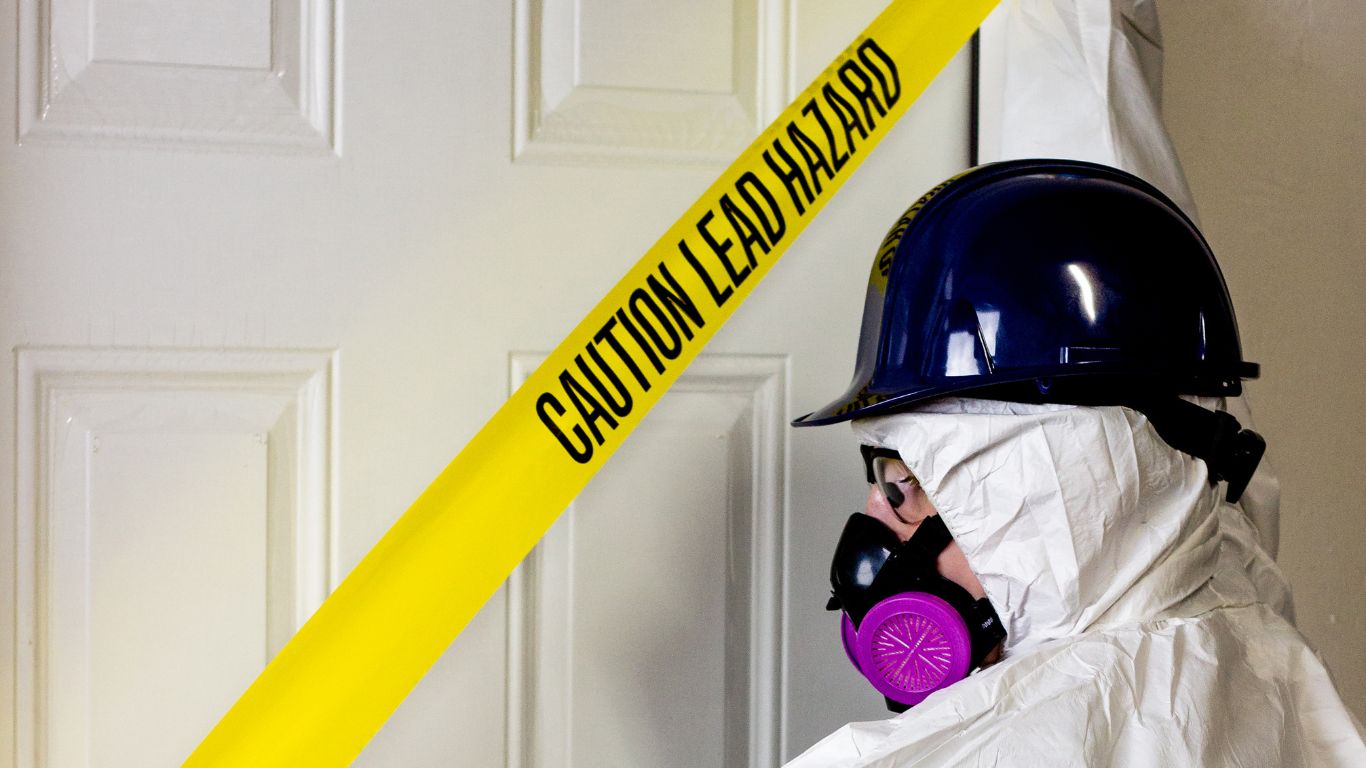Worker in protective gear behind lead hazard tape for lead testing.